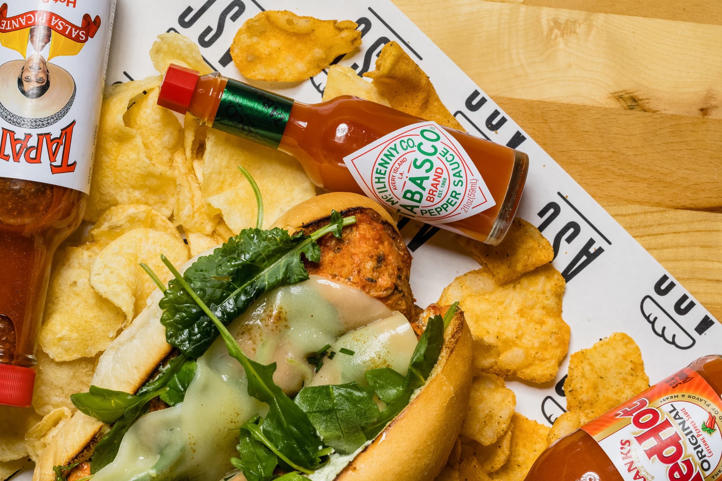 Chicken meatball sandwich with potato chips and a selection of hot sauces