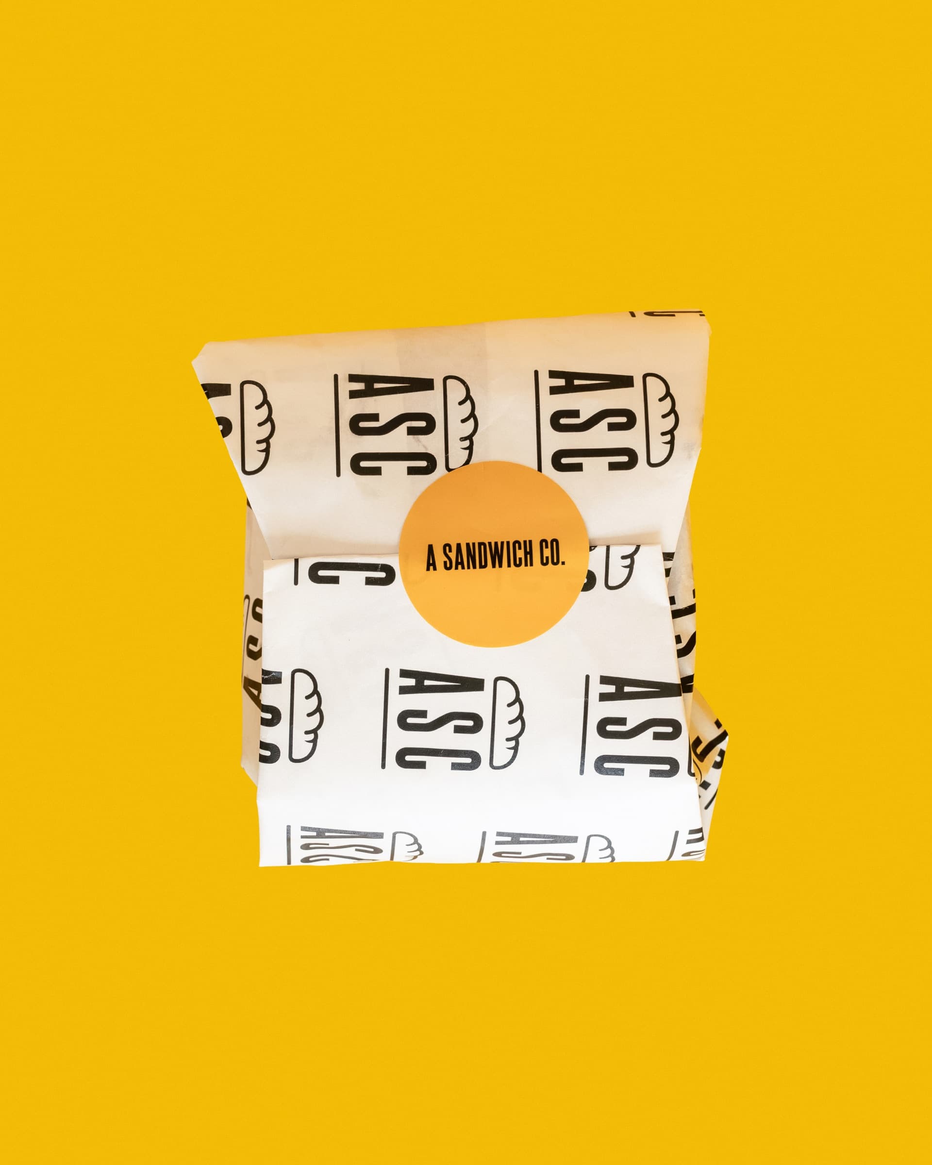 A wrapped A Sandwich Co. order against a bright yellow background