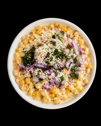 Esquite topped with red onion, cilantro, Tajín, and Cotija cheese