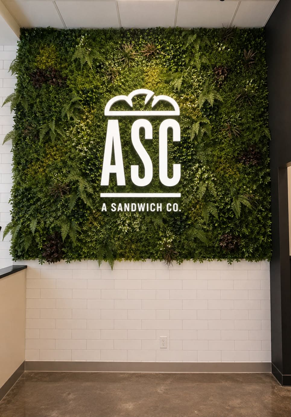 Green living wall with an illuminated A Sandwich Co. logo